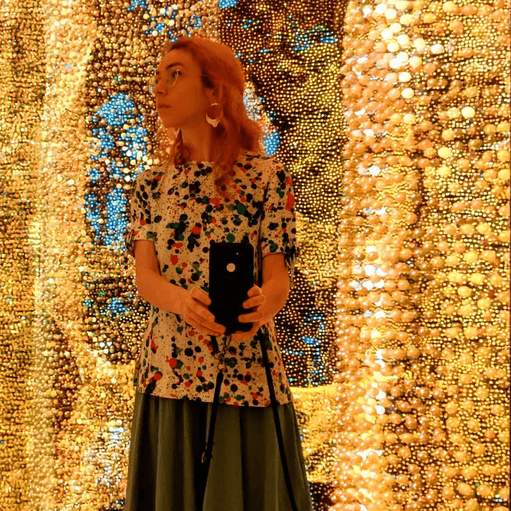 A young woman standing in a room full of lights and mirrors